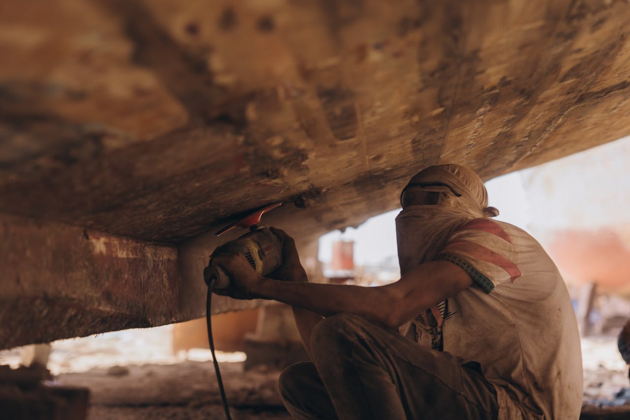 A craftsman at work under a boat in Kafr El-Shaikh, Egypt, showcasing traditional boat repair skills.